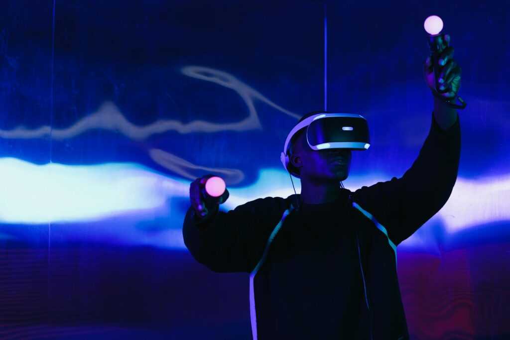 An adult male uses a VR headset and controllers in a futuristic setting with blue lighting.
